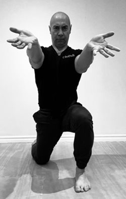 man in exercise clothes resting on left foot, knee bent, with right leg stretched out behind him and both arms reaching forward, palms up