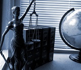 black and white photo of a statue of lady justice bearing sword and scales, next to a globe, on a desk