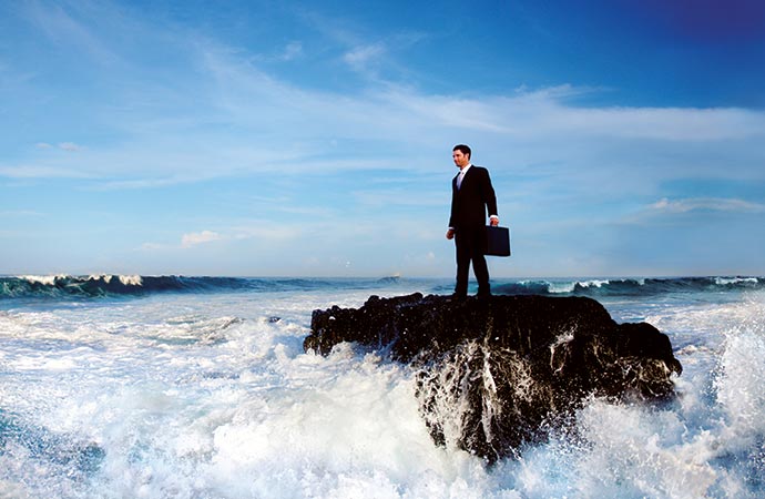 man in a suit standing on a rock in middle of lake, waves crashing around him