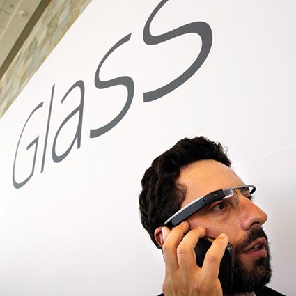 Man wearing Google glasses under a sign that reads GLASS