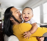 A young man lifts up baby in his arms as they both smile