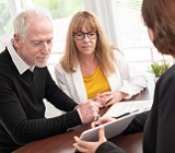 an older man and woman couple meet with an estate lawyer at a desk as she shows them information on a tablet