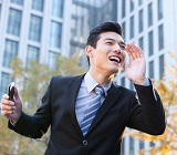 business man in front of fall trees and tall builds call excitedly across the street