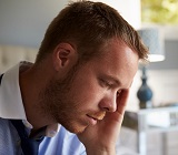 Man in shirt and tie getting ready for work and looking nervous, head in hand