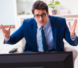 man in blue suit looking at television with hands up in frustration