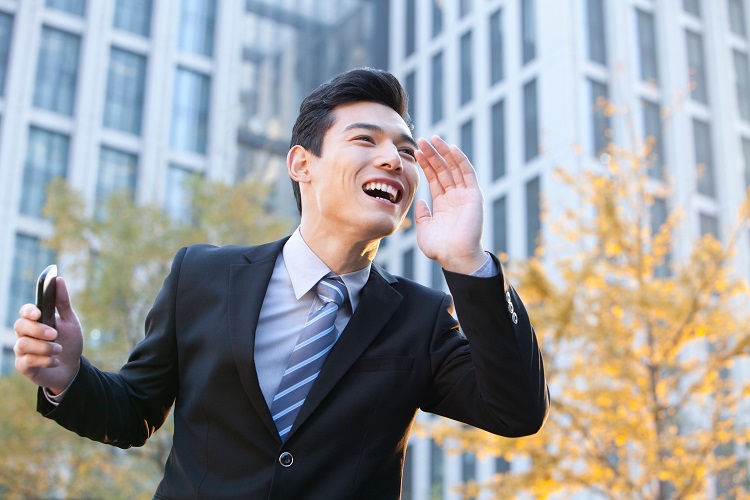 business man in front of fall trees and tall builds call excitedly across the street