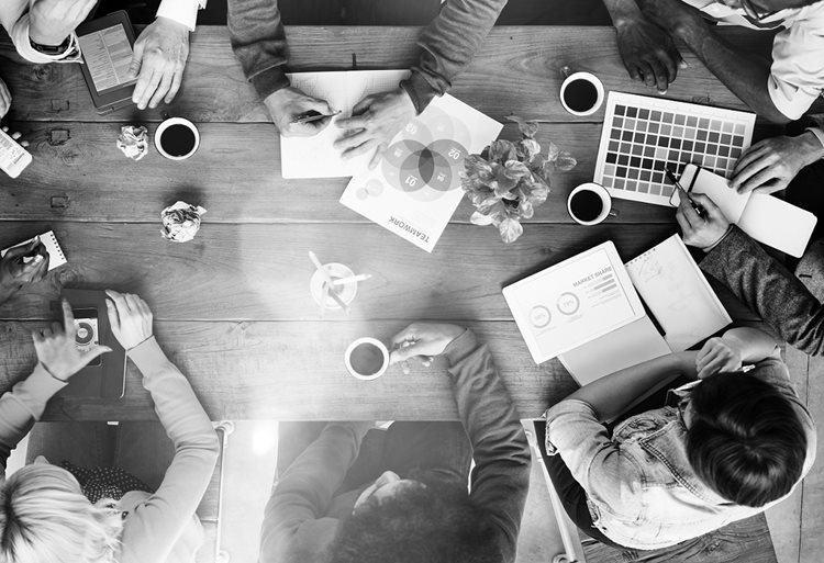 Black and white photo of people gathered around table with coffees