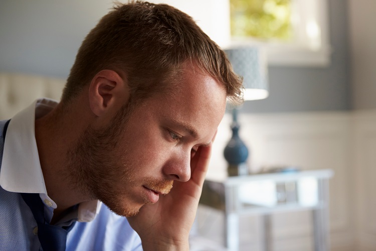 Man in shirt and tie getting ready for work and looking nervous, head in hand