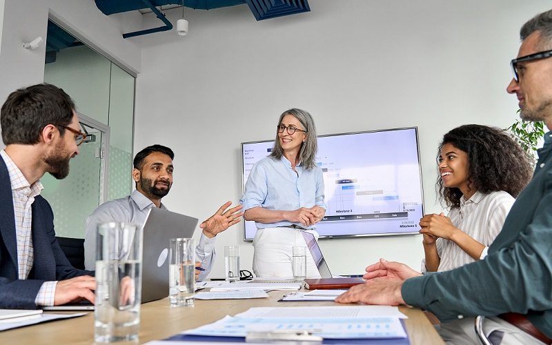 five professionals, of diverse races, genders and ages, discuss business over meeting table