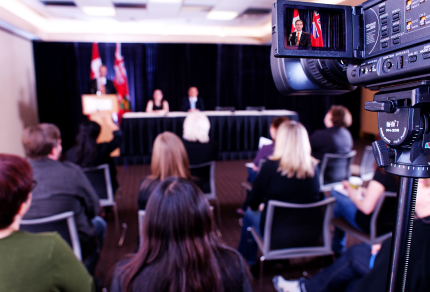 Camera with audience and head table in background.