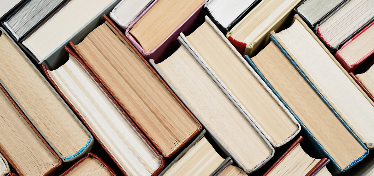 A creative arrangement of books stacked in a diagonal pattern, showcasing their spines and pages in neutral tones.
