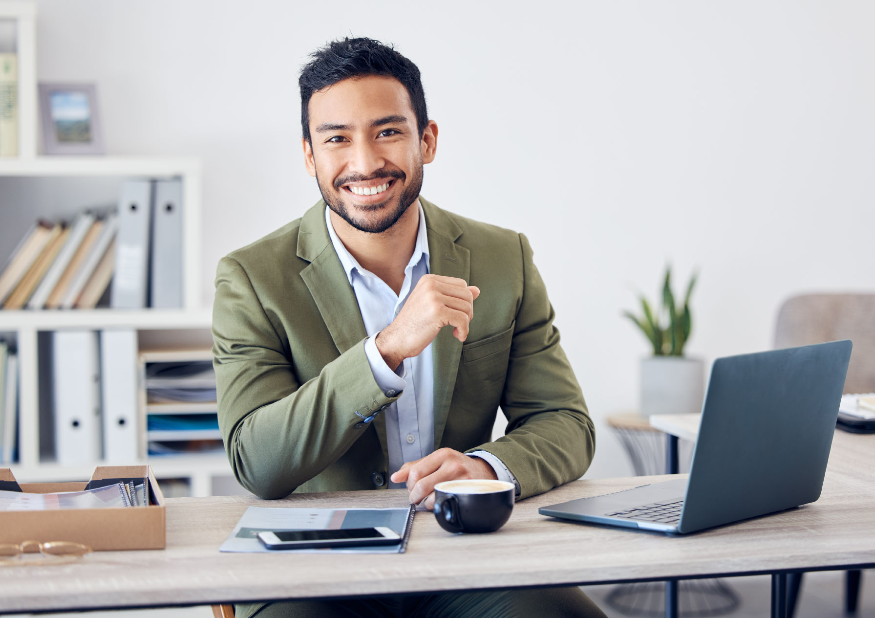 Smiling man sitting at a desk with a laptop, calculator, and documents