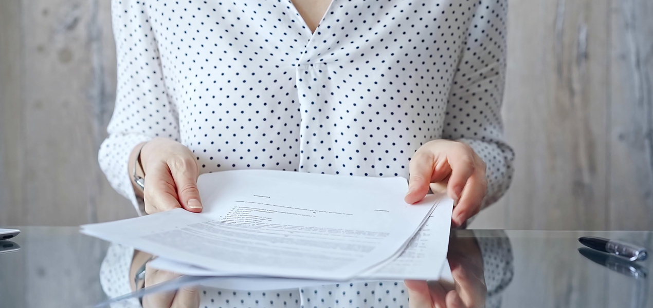 A professional reviewing a stack of documents on a desk, symbolizing guidelines, terms of reference, or official paperwork.