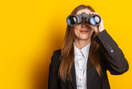 Smiling young professional holding binoculars against a bright yellow background, symbolizing career opportunities, future planning, and professional growth.