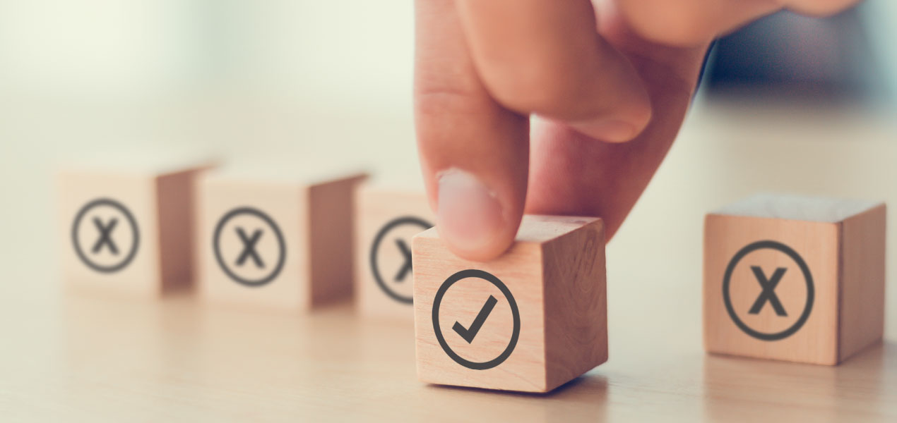 Hand selecting a wooden block with a check mark symbol among several blocks with X marks, symbolizing making the right choice or decision