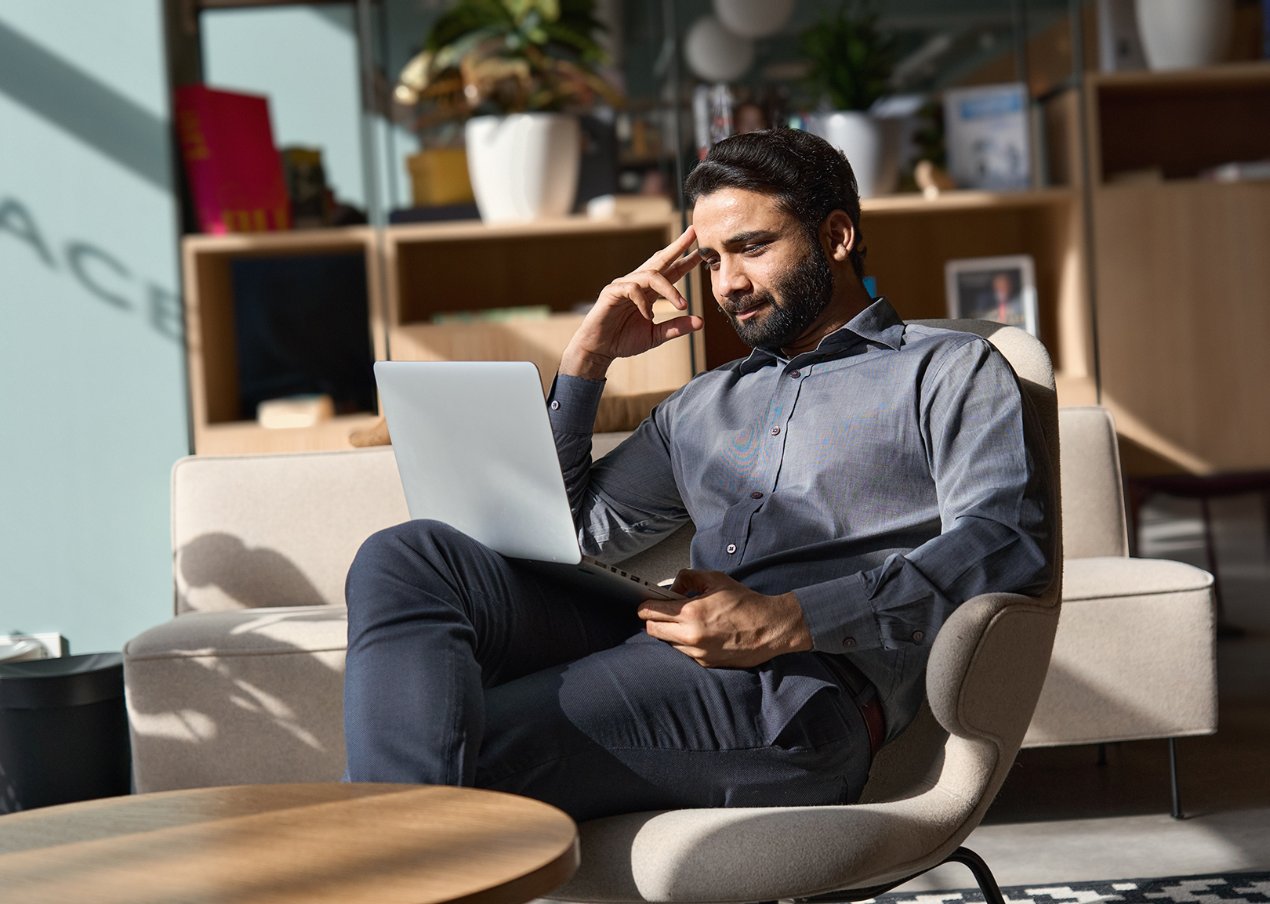 A man sitting in a modern, well-lit workspace, thoughtfully working on his laptop