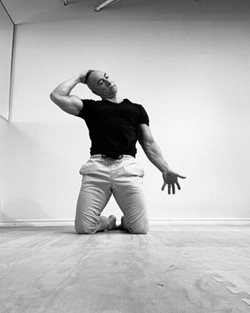 man in exercise close kneeling on floor with right arm bent and supporting his head and left arm stretched forward, palm up